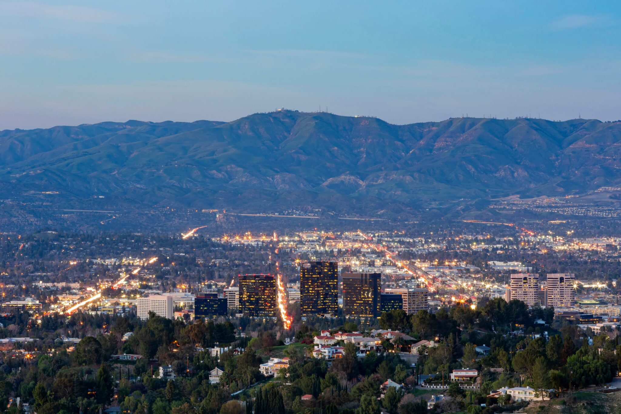 City skyline at dusk with a distant mountain range and illuminated streets below.